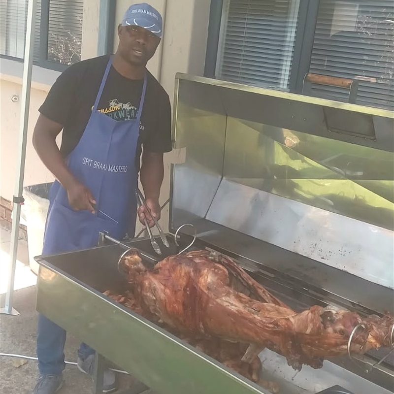 A Spitbraai Masters chef in a branded apron working a whole lamb on the spit