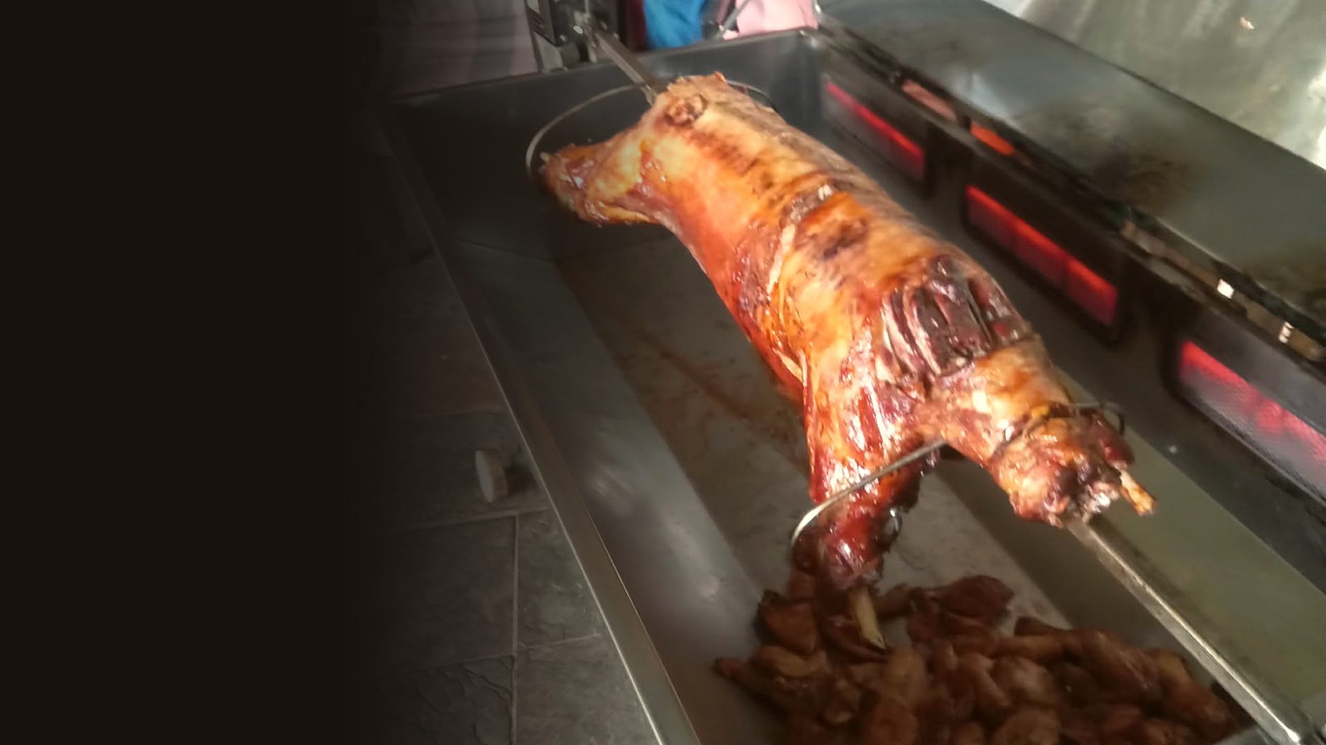 A whole lamb roasting on a Spitbraai Masters spit, with roast potatoes in the drip tray below